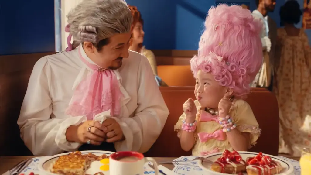 Pembe peruklu küçük kız ve kostümlü adam, IHOP masasında çilekli dolgulu Fransız tostu önünde reklam sahnesinde