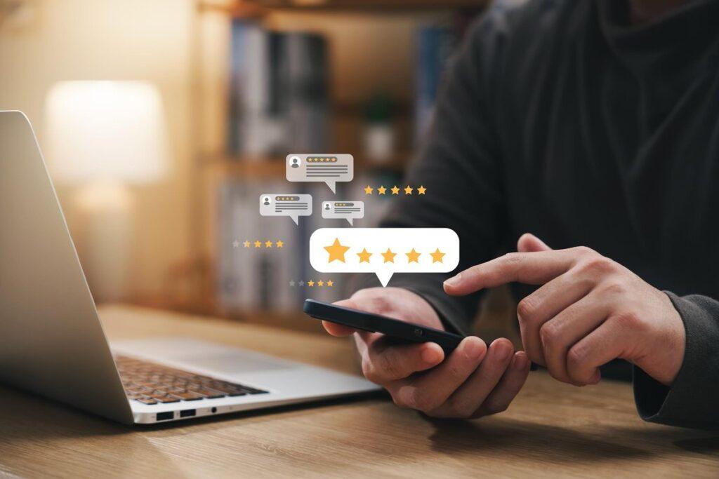 Dizüstü bilgisayar başında akıllı telefondan beş yıldızlı müşteri yorumu veren bir kişinin elleri